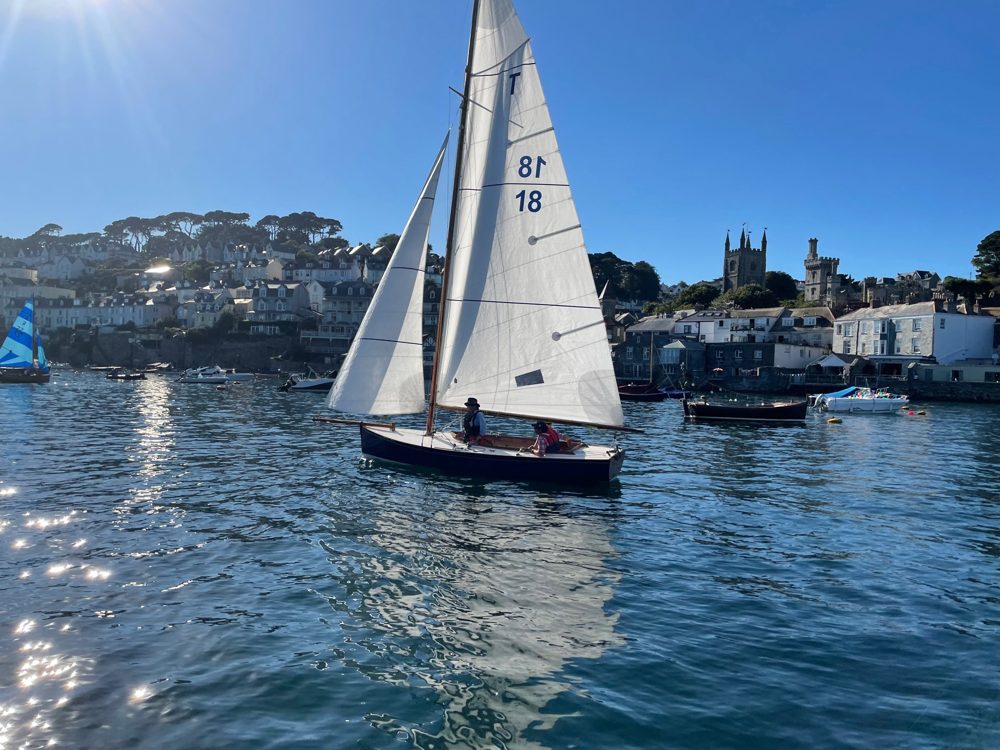 A sailing boat crossing a Cornish harbour